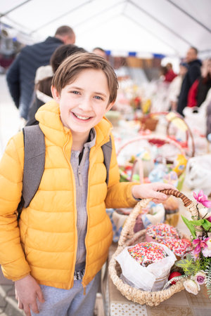 happy 11-year-old boy stands near a basket with Easter cakes and colored eggs. a child with Easter...