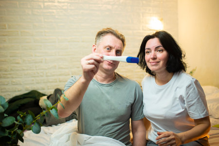 Woman and man with a pregnancy test in the bedroom at home.
