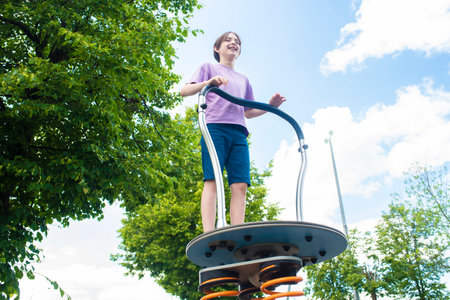 happy 11 year old boy playing on the balance board on the playground in the parkの写真素材