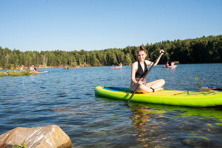 teenage girl or young woman on a SUP, paddle board on a beautiful lake in summer.