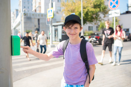the boy presses the traffic light button, stands in front of the pedestrian crossing, is about to cross the roadの写真素材