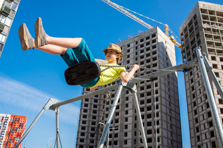 An 11 year old boy, a teenager, swings on a swing in front of a residential complex under construction.の写真素材