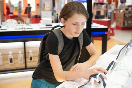 An 11 year old boy with a backpack chooses a mobile phone for himself in a tech store.の写真素材