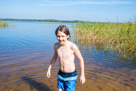 smiling boy in swimming shorts coming out of lake after swimmingの写真素材