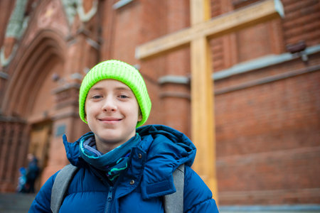 Portrait of a 12 year old smiling boy in a hat and jacket in front of a Catholic church.