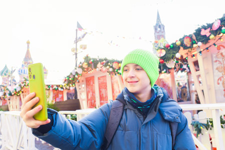 A teenage boy takes a selfie on a smartphone at the Christmas festival "Winter in Moscow" on Red Square near the Kremlinの写真素材