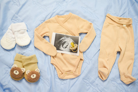 ultrasound photo of baby and pacifier on beige newborn clothes, on blue blanket, top viewの写真素材