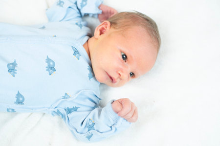 Cute newborn baby boy in blue dress lying on white blanket.