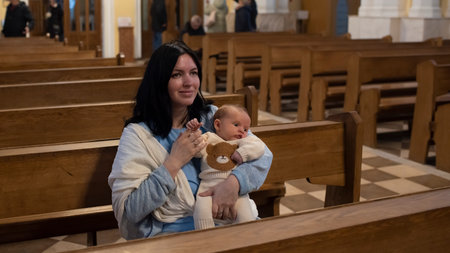 A woman holds a baby boy and sits on a bench in a Catholic church.