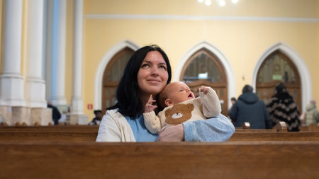 A woman holds a baby boy and sits on a bench in a Catholic church.