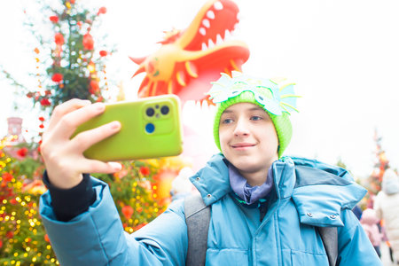 Teenage boy takes selfie with red dragon in background at Lunar Chinese New Year festival in Moscowの写真素材