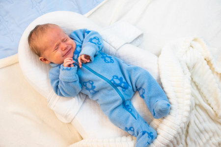 Baby boy crying lying in nursery cocoon for newborns.,Baby is 1 month old.