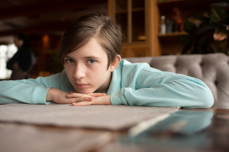 A 12 year old boy sits at a table, resting his head on his hands.