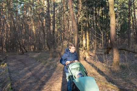 A 12 year old boy walks with a stroller with his younger brother, in the park in early springの写真素材