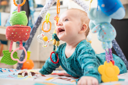 happy 3 month old baby lies on his tummy on a developmental play mat with toys hanging on the arc of the matの写真素材