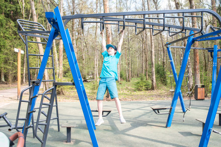 boy by his hands and moving along a hanging horizontal ladder (monkey walker) on a sports ground