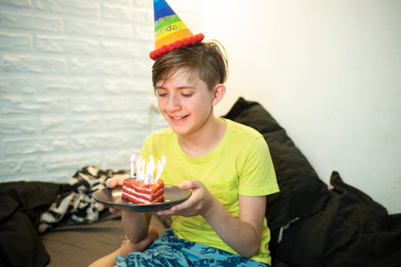 Happy little adorable boy celebrates his birthday. The boy looks at a piece of cake with candles, makes a wish and is going to blow out the candles.の写真素材