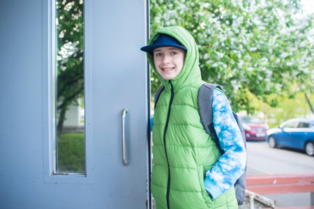 a boy opens the door to the entrance in spring, the child returns from school in spring alone