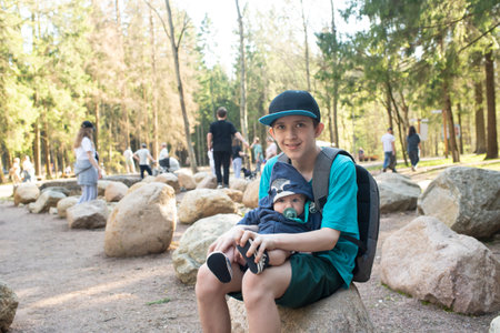 A 12 year old boy holds his baby brother while sitting on a large rock in Borovskoy Park in Moscowの写真素材