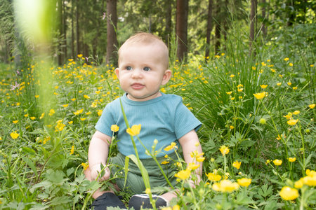 Baby boy sitting on grass surrounded by blooming yellow wildflowers in park in spring. Child is 6 months old.の写真素材