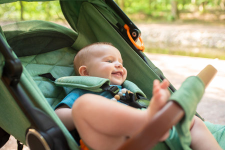 Happy smiling baby boy sitting in green stroller barefoot. Summer in the park.の写真素材