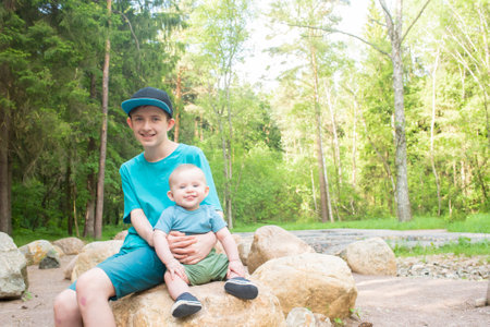 A 12 year old boy holds his baby brother while sitting on a large rock in Borovskoy Park in Moscowの写真素材