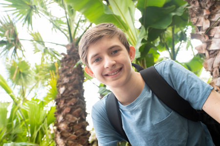 12 year old smiling boy with backpack sits under palm treesの写真素材