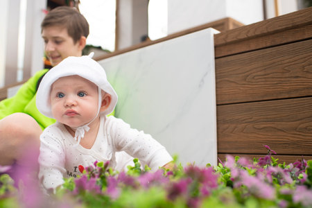 A baby boy crawls on a bench next to his sitting teenage brother. In the park in the summer.の写真素材