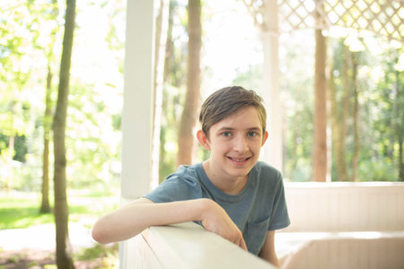 Portrait of smiling 12 year old boy in white gazebo in park in summerの写真素材