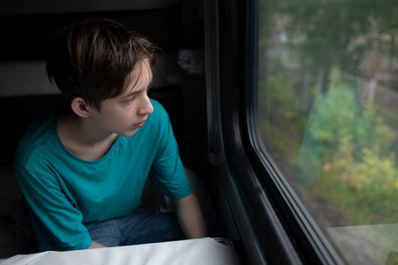 A 12 year old boy sits by the window on a long-distance train in summer.の写真素材