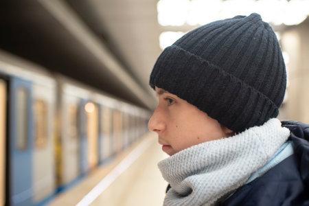 Profile of a teenage boy in a black hat, against the background of a train and a subway platform.の写真素材