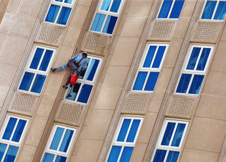 Worker in overalls and a protective helmet washes the windows of an apartment building.の写真素材