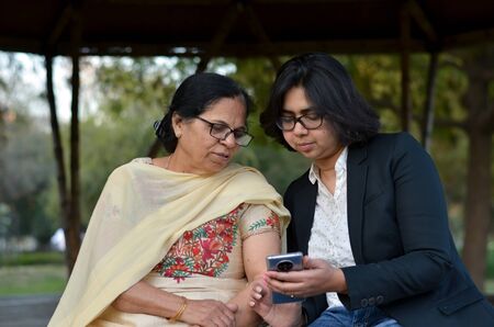 Smart young Indian girl with an old Indian woman looking at the mobile phone and busy talking...