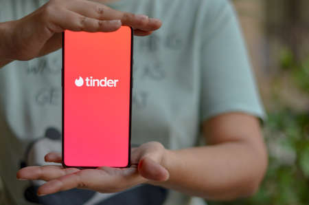 New Delhi, India, 2020. Girl holding mobile with Tinder logo on smartphone screen in female hands. Tinder is a social search and dating mobile appのeditorial素材