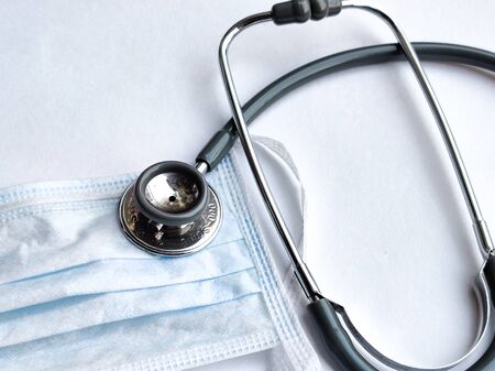 White breathable surgical face mask and stethoscope on a white background denoting doctor's Covid-19 safety kit to reduce the rate of spread of infectionsの写真素材