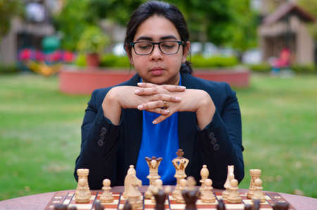 An Indian girl playing chess waiting for the opponent to play and anxiously thinking about her next move. Concept - idea, strategyの写真素材