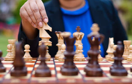 A girl playing chess moving the white knight forward on a chess board with knight picked in her hands. Concept - idea, strategyの写真素材