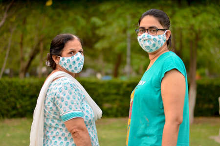 Close up Portrait of a senior Indian lady and young lady wearing matching surgical cotton mask to protect themself from Corona Virus (COVID-19) pandemic in a park in New Delhi, Indiaの写真素材