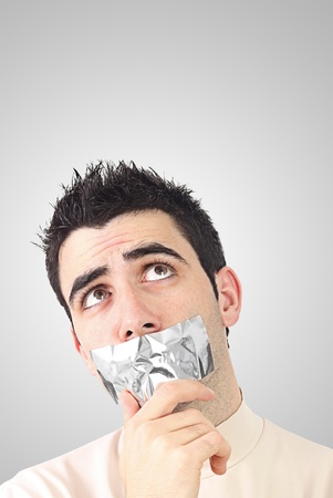 Curious young man having gray duct tape on his mouth.Gradient background with copy space.の写真素材