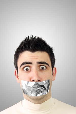 Scared young man having gray duct tape on his mouth.Gradient background with copy space.の写真素材