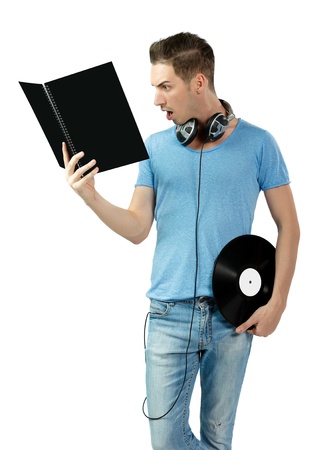 Portrait of suprised young deejay in blue shirt holding a vinyl and learning from black book  Copy space for text  Isolated on white の写真素材