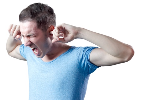 Young man yelling with fingers in ears, wearing blue shirt. White background.の写真素材