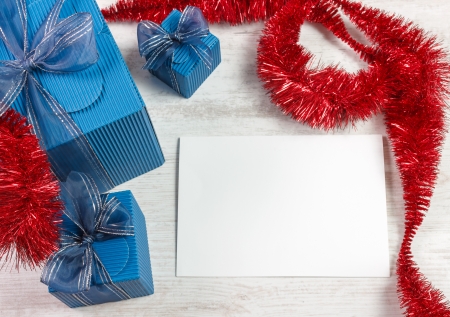 Christmas decoration with three blue gift boxes and red garland against wooden white table  White paper with copy space for your best wishes の写真素材