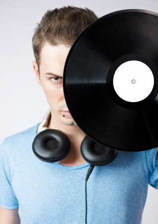 Serious young man covering his face with a vinyl disc against grey background.の写真素材