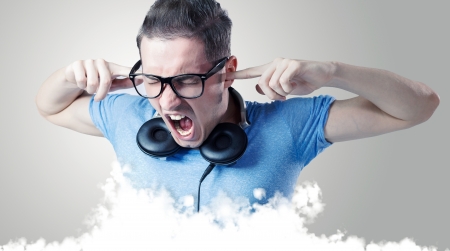 Young man with headphones and black glasses yelling with eyes closed above some white clouds.の写真素材