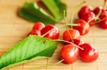 Group of cherries placed near green leaf on bamboo tablecloth.Small depth of field with cross processing.の写真素材