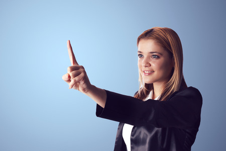 Smiling business woman pointing to empty space on the left side of the photo. Blue background.の写真素材