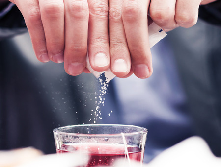 Close-up of white sugar particles falling in cup filled with tea.の写真素材