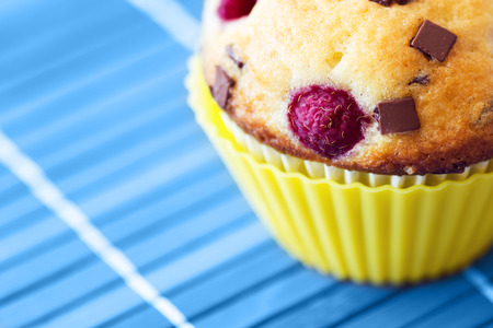 Tasty muffin with raspberry and chocolate. Blue wooden tablecloth as background.の写真素材