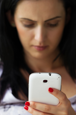 Depressed woman texting on white smartphoneの写真素材